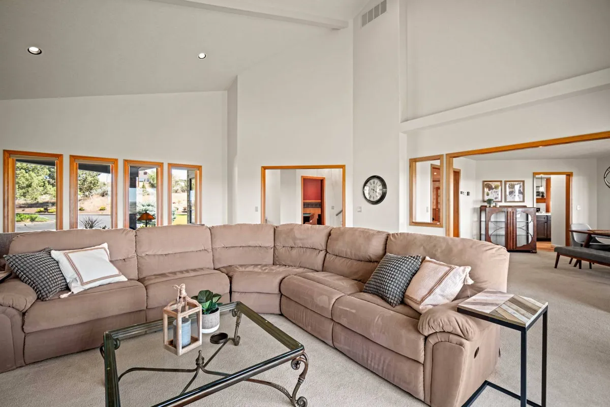 A cozy and welcoming interior scene with a sectional sofa, large windows letting in natural light, a glass coffee table, and decorative items. The space feels comfortable and inviting, ideal for relaxing with pets after outdoor adventures.