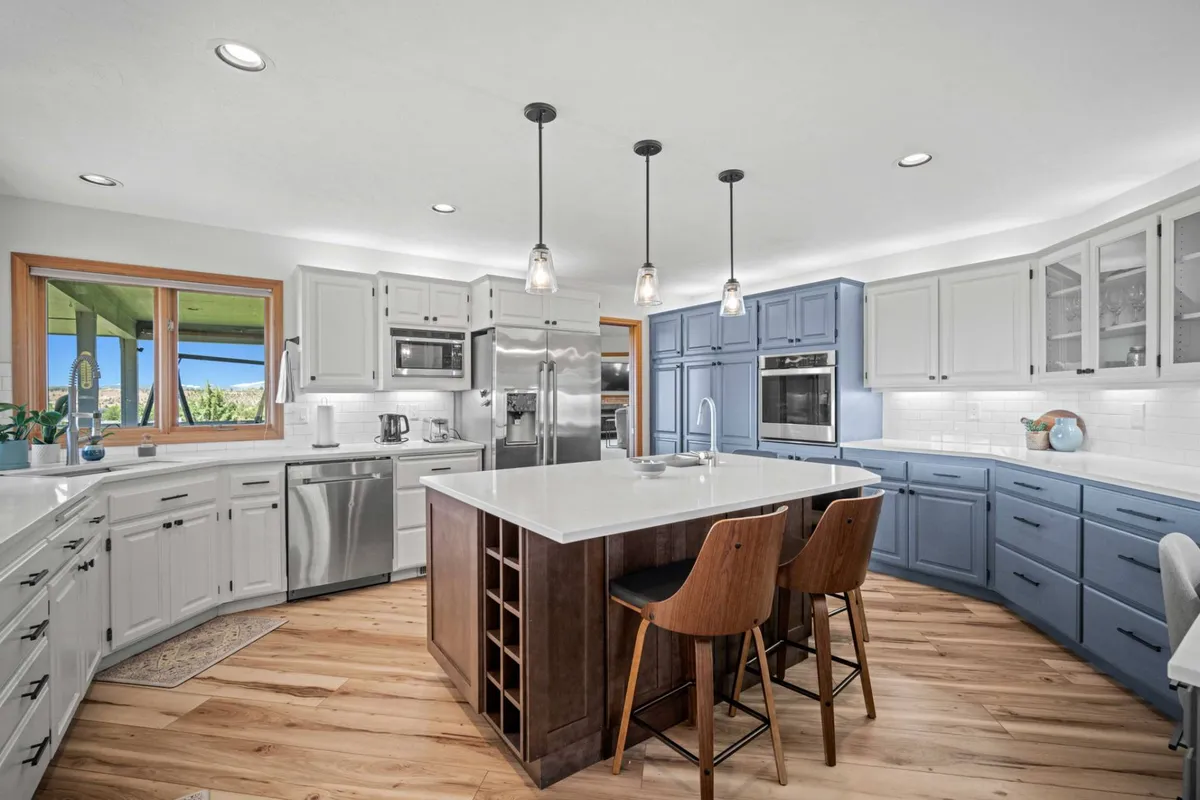 A contemporary chef’s kitchen with a spacious central island, striking blue cabinetry, and warm wooden floors. The open design and generous workspace are ideal for culinary gatherings, with plenty of room for conversation and participation while cooking.