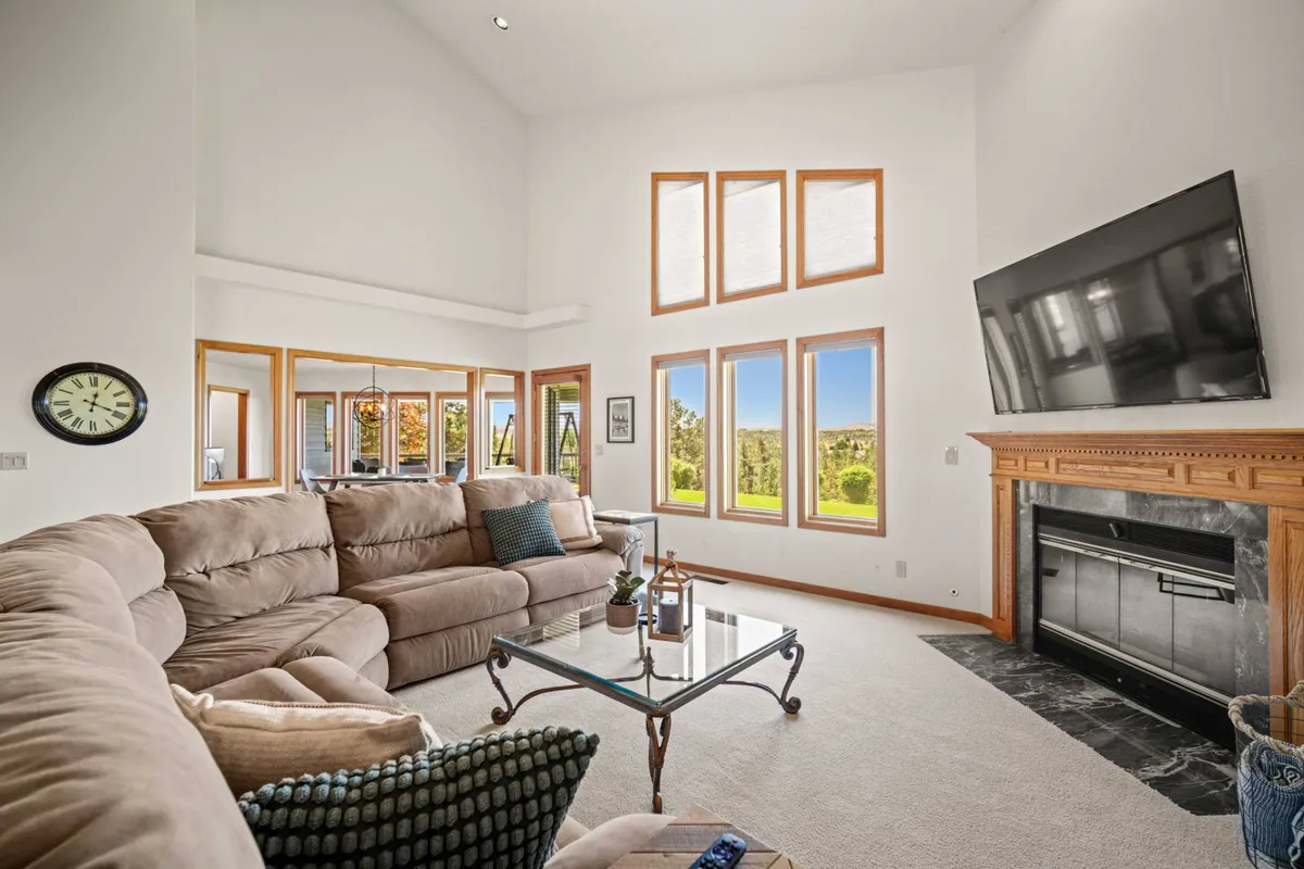 A spacious living room featuring a large sectional sofa positioned to maximize enjoyment of the floor-to-ceiling windows, which offer sweeping valley and mountain views. The inviting fireplace and a television add both warmth and entertainment, while the open layout encourages relaxation and socializing.
