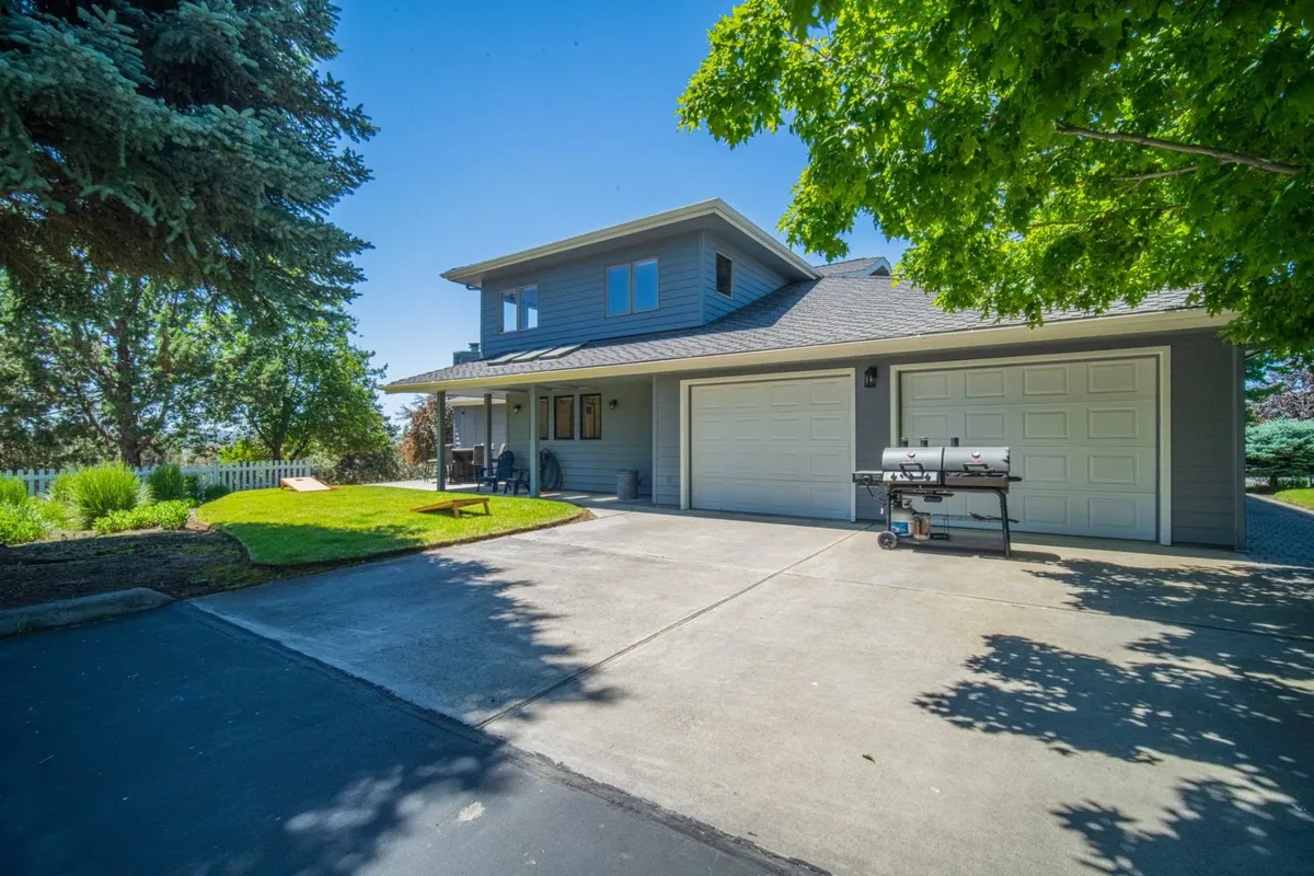 This exterior image features the front porch, lawn area, driveway, and garage doors of the property. There is also a grill visible, suggesting opportunities for outdoor dining or barbecuing. The porch and yard provide ample space for relaxing or letting pets enjoy the outdoors in a safe, welcoming environment.
