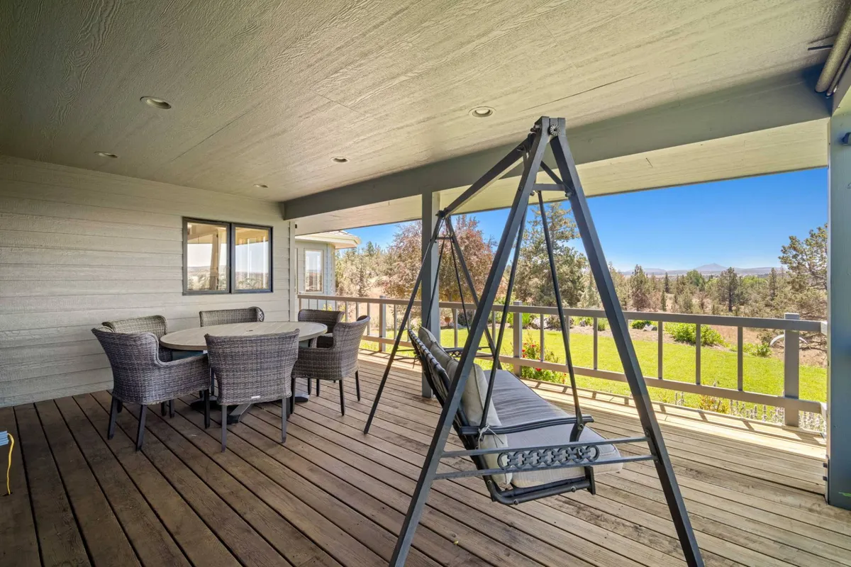 This image spotlights a wooden deck featuring a hanging swing and a generously sized dining table, set against the backdrop of a tranquil outdoor environment. The seating arrangement and swing are focal points, inviting guests to relax or gather together. The subtle glow of evening light suggests a peaceful, versatile space perfect for morning coffee or sunset happy hour.