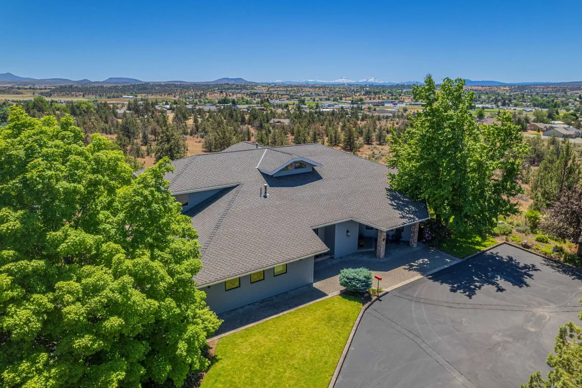 This exterior shot captures the house nestled among trees with a sweeping view of the valley and distant mountains in the background. The driveway leads up to the home, and the surrounding natural landscape hints at plentiful opportunities for outdoor activities and relaxation.