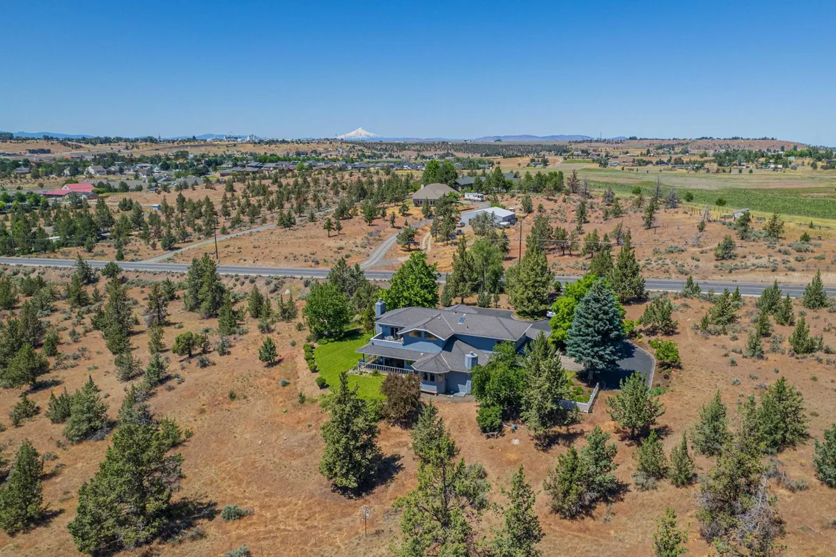 This exterior image captures the large house set against a backdrop of surrounding trees and open land, with distant mountains visible. The scene exudes serenity and connection to nature, and hints at the tranquility available after a day of adventure.