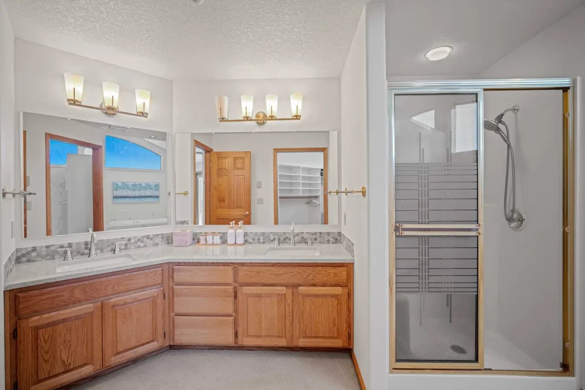 A modern bathroom with a double vanity, large mirrors, a spacious shower area, and warm wooden cabinetry. The design is contemporary and functional, providing a welcoming space for personal routines and self-care.